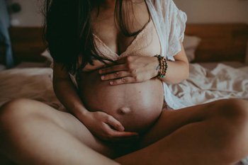 a pregnant woman sits on a bed and gently holds her belly